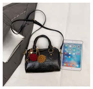 Detail view of small black patent leather barrel bag with gold hardware and accessories