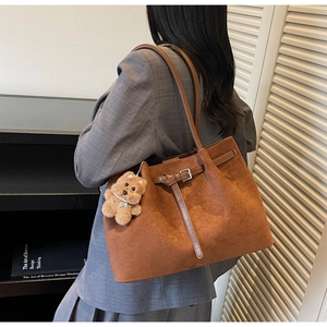 Detail of warm brown suede tote bag with decorative buckle and plush bear pendant