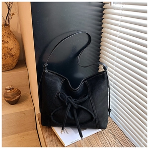 Close-up of black suede shoulder bag with contrast stitching on wooden table