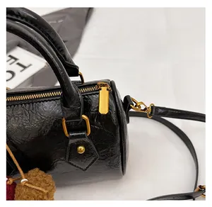 Close-up of a black cylinder bag featuring vintage pleated texture and gold hardware