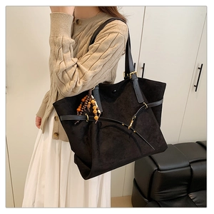 Detail of black suede tote bag featuring ethnic beaded tassel and gold buckle accent