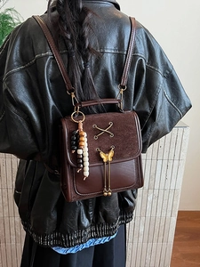 Vintage dark brown leather backpack with bow metal detail and beaded charm in a lifestyle shot