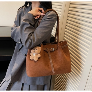 Close-up of brown suede tote bag featuring leather straps and a cute teddy bear charm