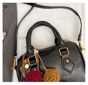 Close-up of a retro black cylinder bag with golden buckles and plush pompom detail