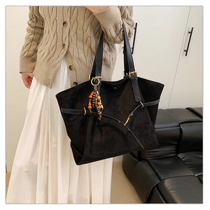 Detailed view of black tote bag with beaded charm and decorative straps for commuting