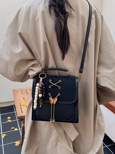 Minimalist black leather backpack with gold bow buckle and wooden bead charm accessory