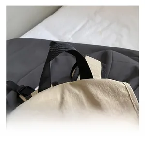 Détail du sac à dos en nylon beige montrant la poignée en sangle noire et les coutures