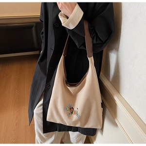 Detail of beige canvas hobo bag featuring colorful animal embroidery and brown leather strap