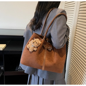 Detail of brown suede tote bag with plush bear charm and decorative buckle strap