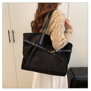 Detailed view of a large black suede tote bag with leather straps and gold metal buckles