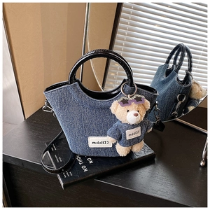 Dettaglio della borsa a secchiello in denim con charm orsetto e manici neri lucidi