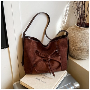 Detail of retro brown suede tote bag with large bow and contrast stitching on books