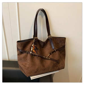 Detail of dark brown suede tote bag with leather straps and retro beaded charm on a chair