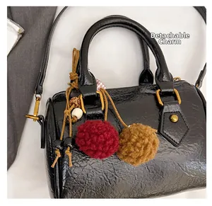 Detail of black litchi texture boston bag with a colorful plush detachable charm