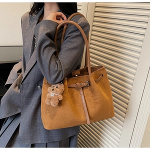 Close-up of brown suede tote bag with metal buckle and plush bear charm on a grey suit