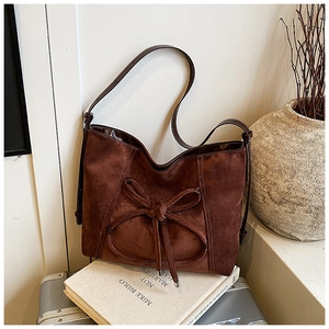 Détail du sac à bandoulière en daim marron foncé avec un nœud décoratif sur le devant