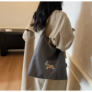 Detail of grey canvas tote bag with colorful zebra embroidery worn with a beige trench coat