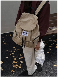 Outdoor shot of beige drawstring backpack with side zip pockets and a woven label detail