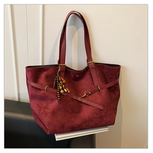 Detail of burgundy suede tote bag with leather straps and decorative beaded pendant detail