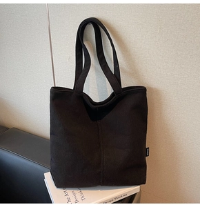 Detail of black corduroy tote bag showing soft ribbed texture and side brand label