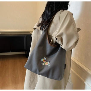 Close-up of grey canvas tote bag featuring colorful zebra embroidery and brown leather trim