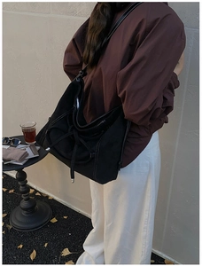 Détail du sac hobo en daim noir avec coutures contrastées et cordon décoratif