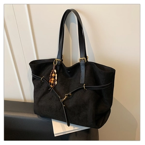 Detail of black suede tote bag featuring leather handles and wooden bead tassel decor