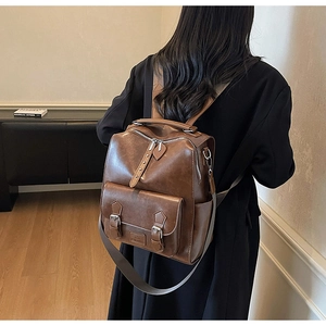 Rear view of model wearing a vintage brown faux leather backpack with metal buckles
