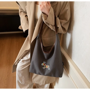 Detail of grey canvas tote with vibrant zebra embroidery and brown leather handle