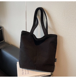 Detail shot of black corduroy tote bag showing side label and soft ribbed fabric texture