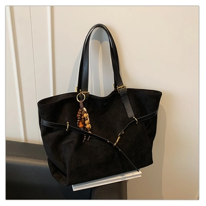 Detail view of black suede tote bag with leather straps and wooden bead charm accent