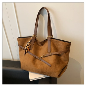 Detail of caramel brown tote bag with leather straps and decorative wooden bead charm