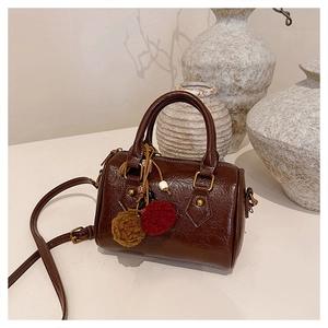 Detail of a dark brown barrel bag with a plush charm and vintage gold hardware accents