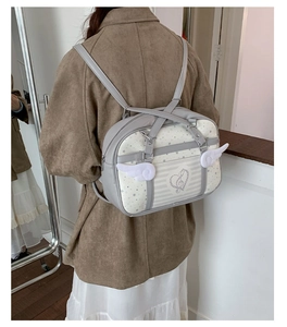 Dettaglio di zaino grigio stile JK con cuore ricamato, note musicali e ali bianche decorative
