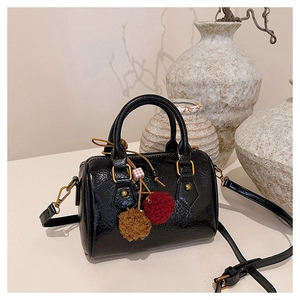 Detail of black patent leather barrel bag with gold hardware and plush ball charms