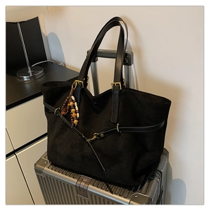 Detail of black matte tote bag with golden buckle and beaded charm on a silver suitcase