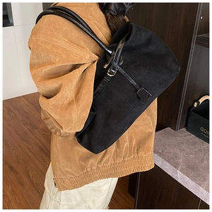 Detail view of a large black suede tote bag styled with a vintage brown jacket