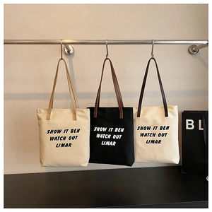 Trois sacs cabas minimalistes en toile avec anses en cuir exposés dans un showroom moderne