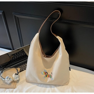 Detail of embroidered animal patch on large off-white canvas tote with brown leather strap