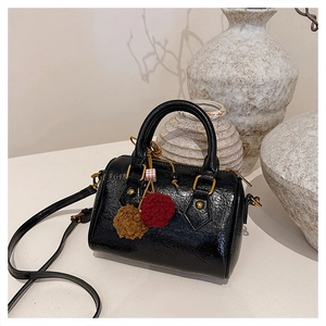 Detail of black cylinder bag with gold hardware and a brown fuzzy pompom charm