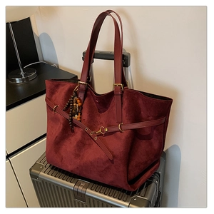 Detail of burgundy suede tote bag with beaded charm on a suitcase for travel
