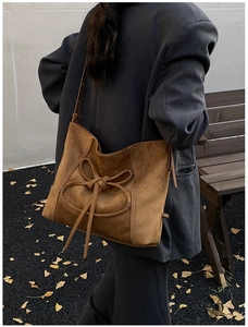 Brown suede tote bag with decorative bow tie shown on model in a retro outdoor setting