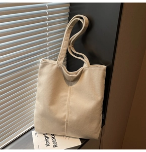 Detail of cream corduroy tote bag showing vertical ribbed texture and brand tag by window