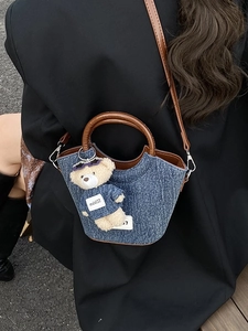Borsa a secchiello in denim blu con manici in pelle marrone e un ciondolo a orsetto