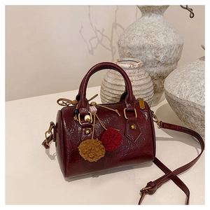 Close-up of wine red Boston bag in pebble leather with gold hardware and fur pompom charm