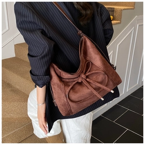 Vue détaillée du sac cabas en daim marron foncé avec nœud décoratif et bandoulière en cuir