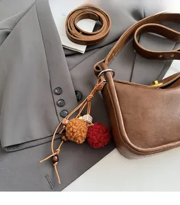 Brown leather shoulder bag detail with plush charm and golden twist lock closure