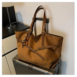 Detail of dark brown suede tote bag with leather handles on a suitcase for travel