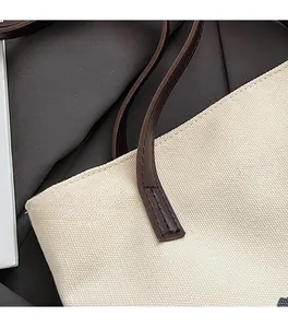 Détail de la poignée en cuir avec double couture sur un sac cabas en toile blanc cassé