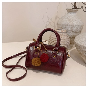 Detail of burgundy patent leather Boston bag with plush pompoms and gold metal hardware